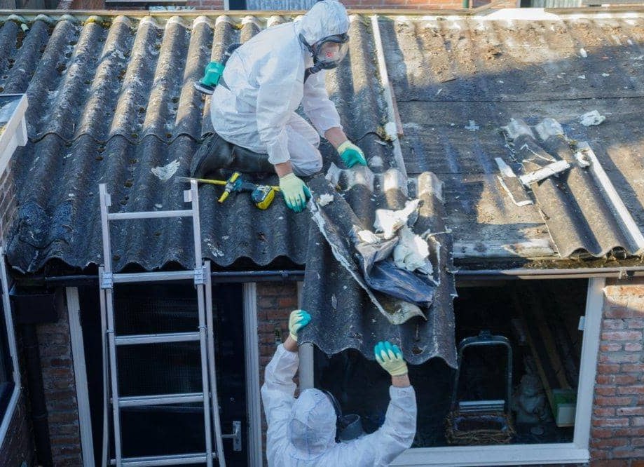 Zwei Mitarbeiter in Schutzanzügen beim Rückbau eines Asbestzementdachs